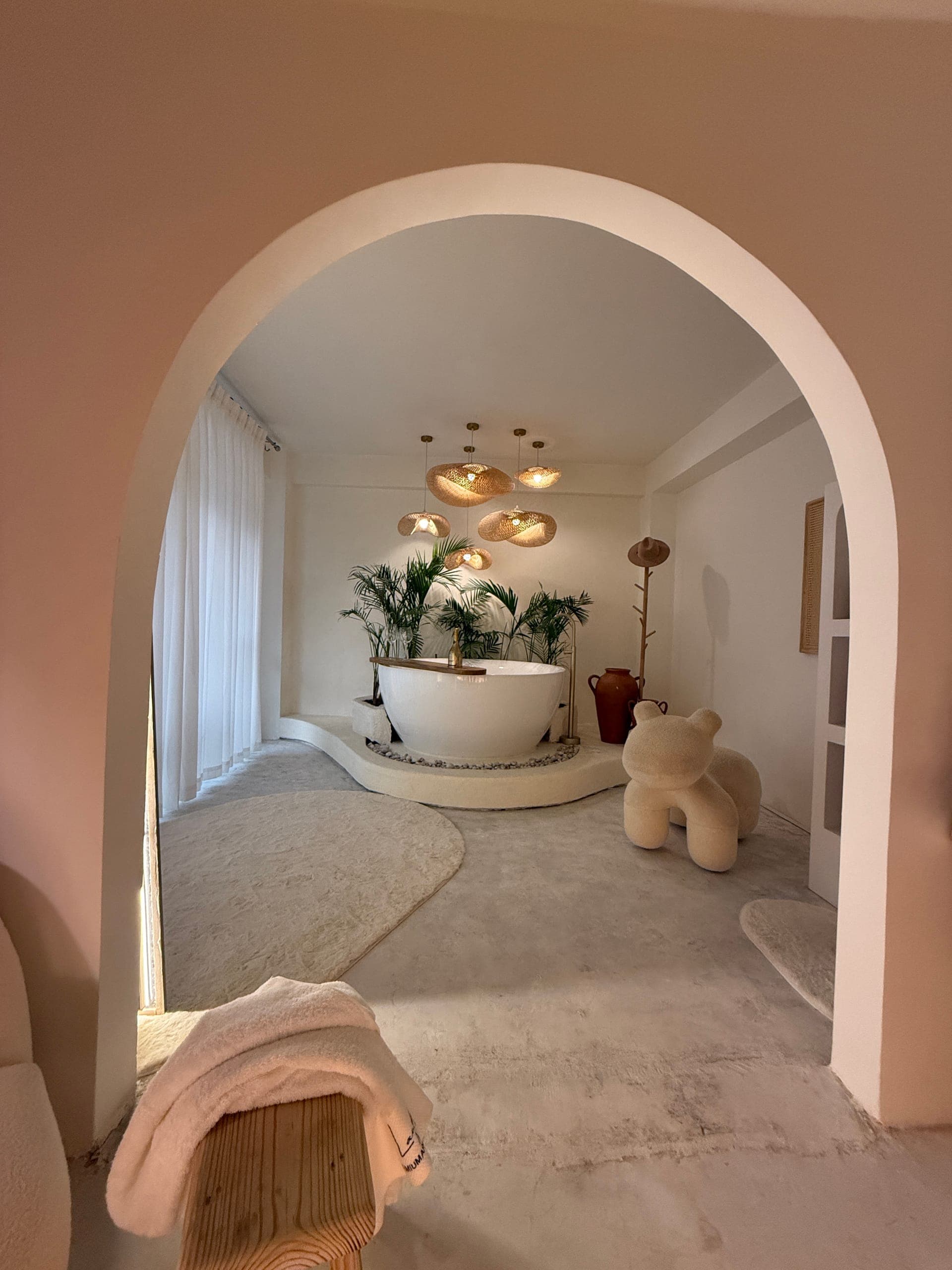 The Presidential Suite bathtub seen through a plaster archway: a freestanding tub on pebbles, palms and bamboo pendants