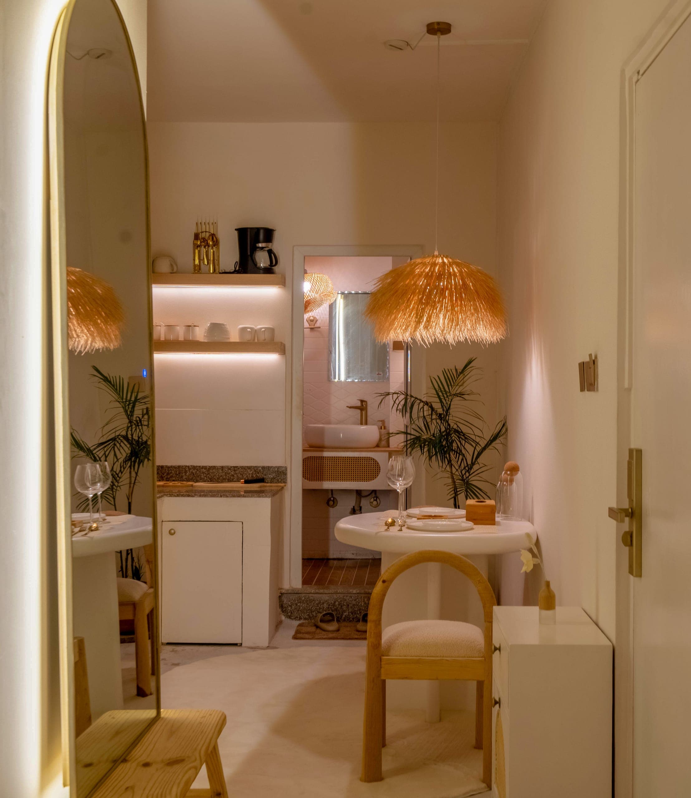 Studio Airbnb at Lagom: an arched mirror, a round table for two, a straw pendant and the kitchenette beyond