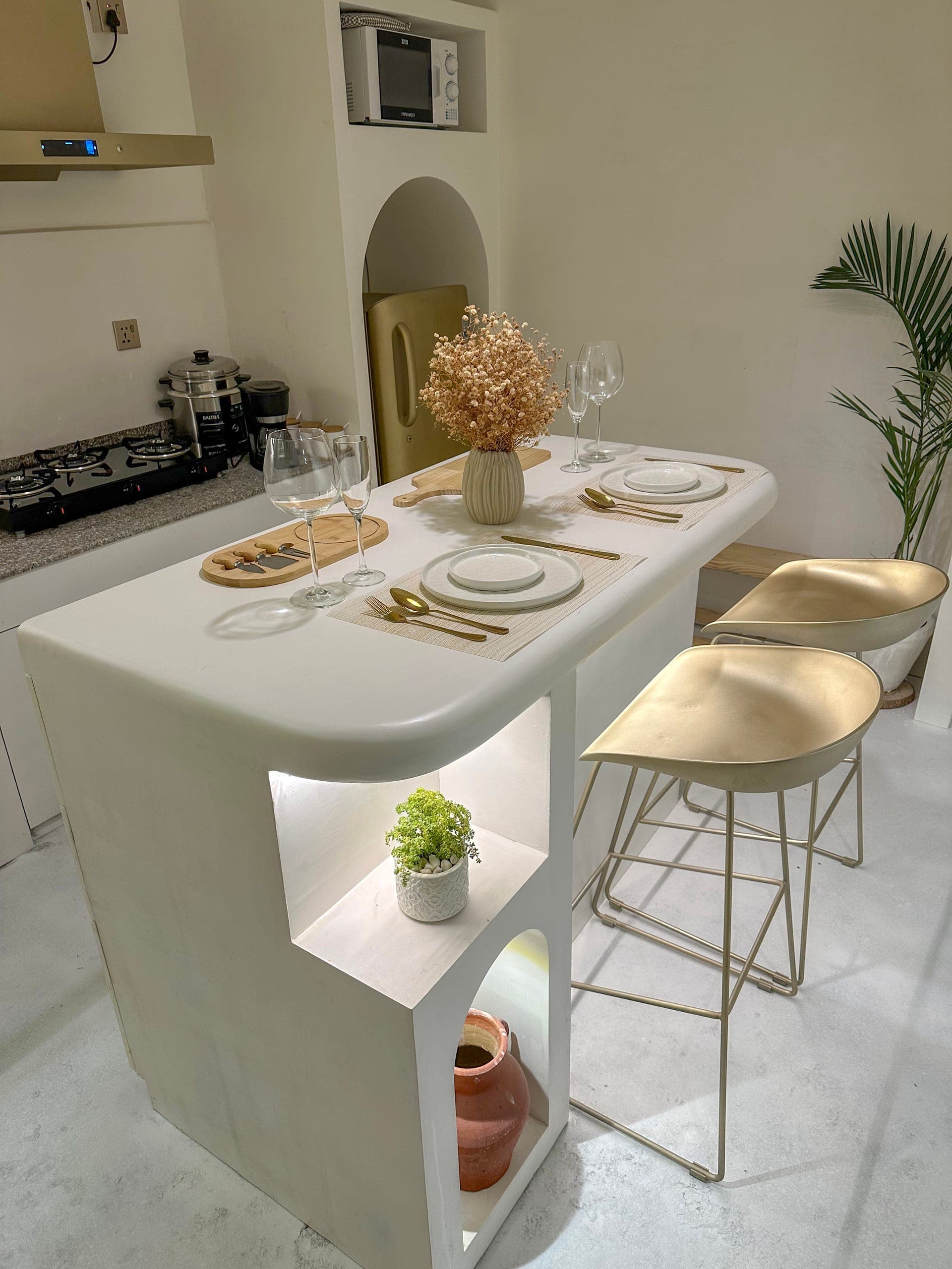 1BK kitchen island set for dinner with gold bar stools, a gold fridge, a microwave and a palm