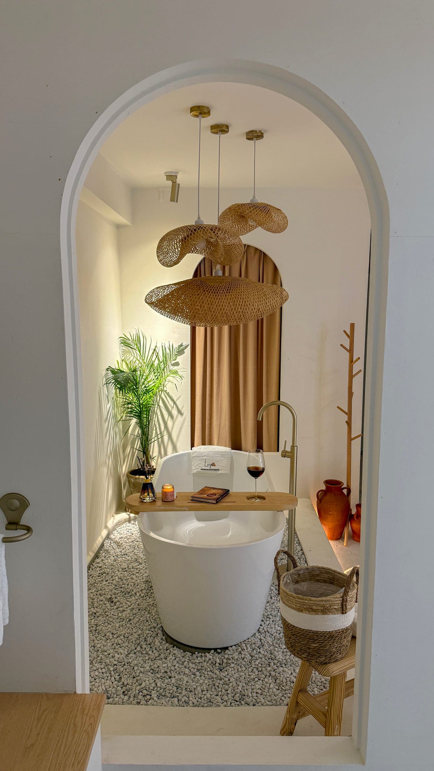 The 2BHK bathtub framed by a plaster archway, with palms, terracotta jugs and an arched curtain