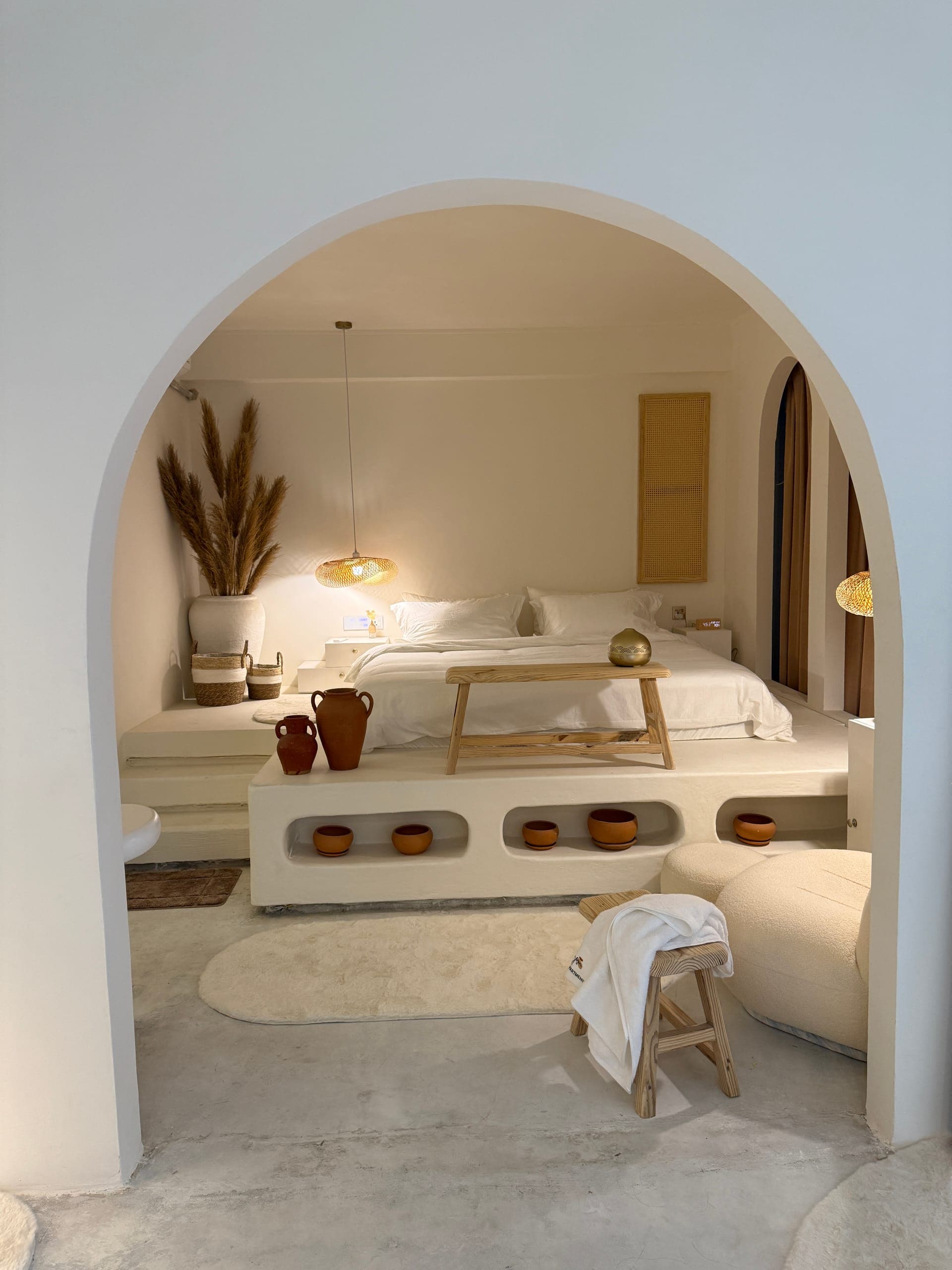 The suite bedroom through an arch: a platform bed with lit niches, a bench and a boucle chair