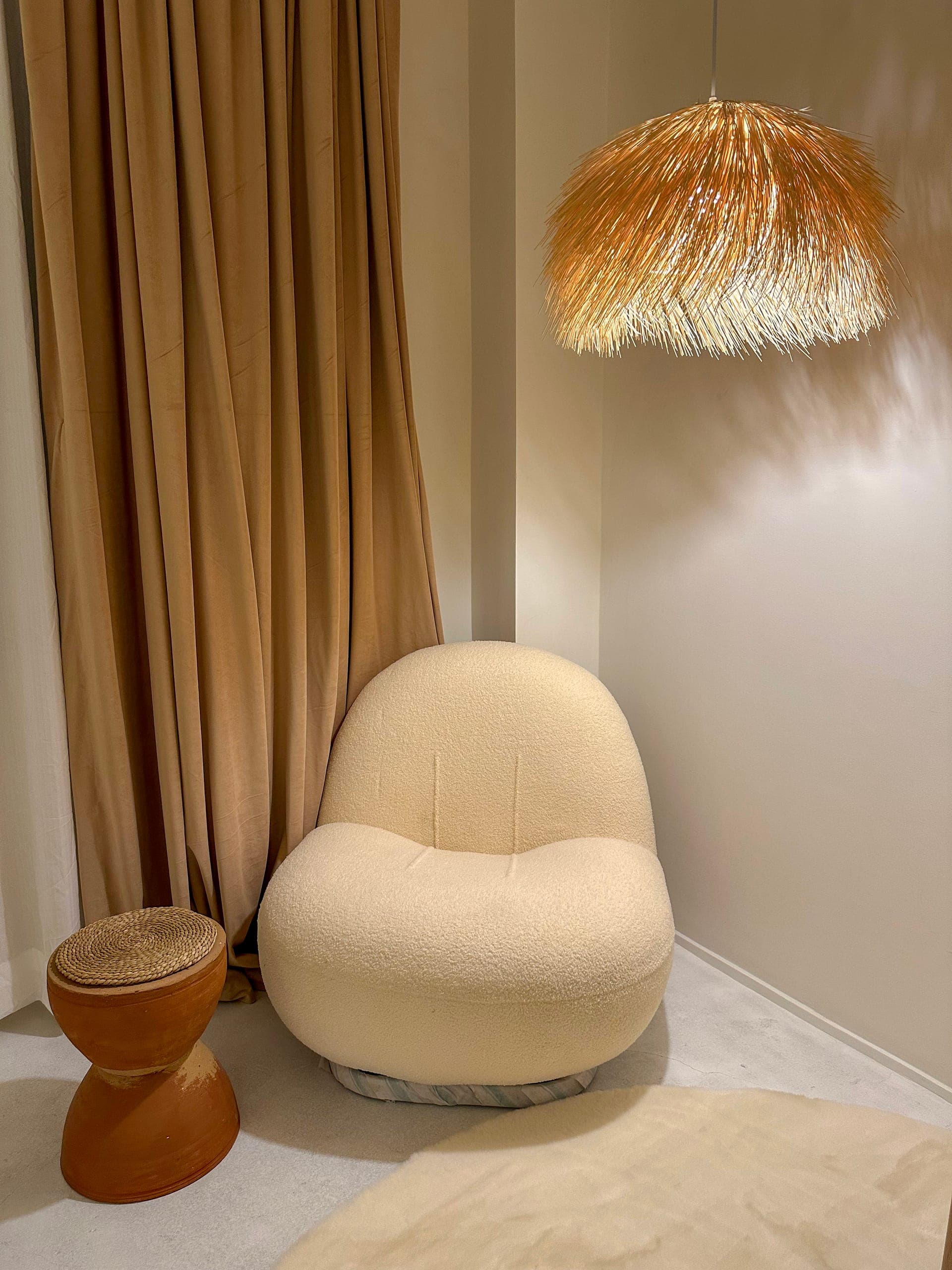 Boucle lounge chair and a terracotta side table beside linen curtains under a straw pendant in the 1BK