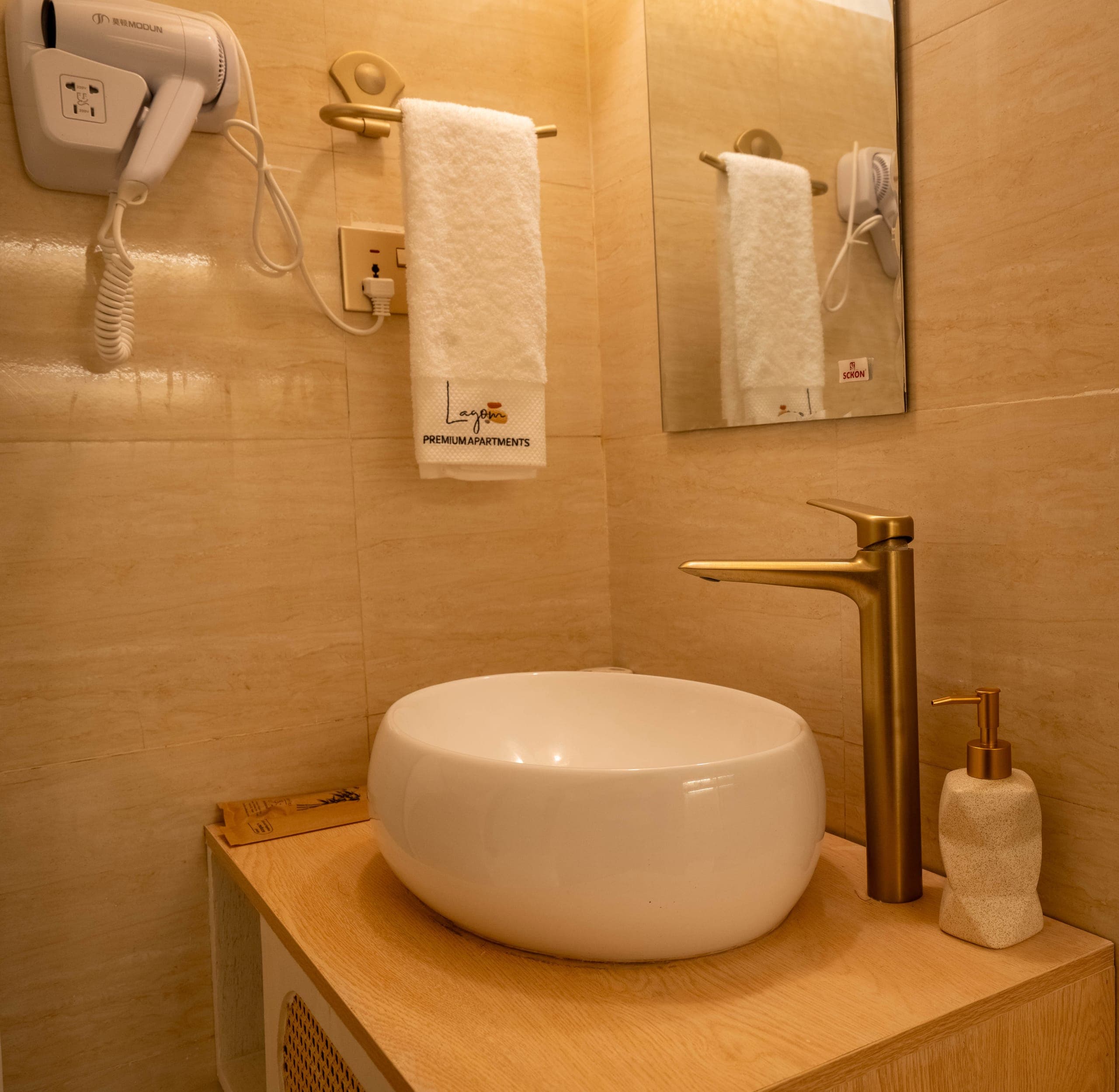 Deluxe bathroom: a round vessel basin with a brass tap on an oak vanity, towels and a hair dryer