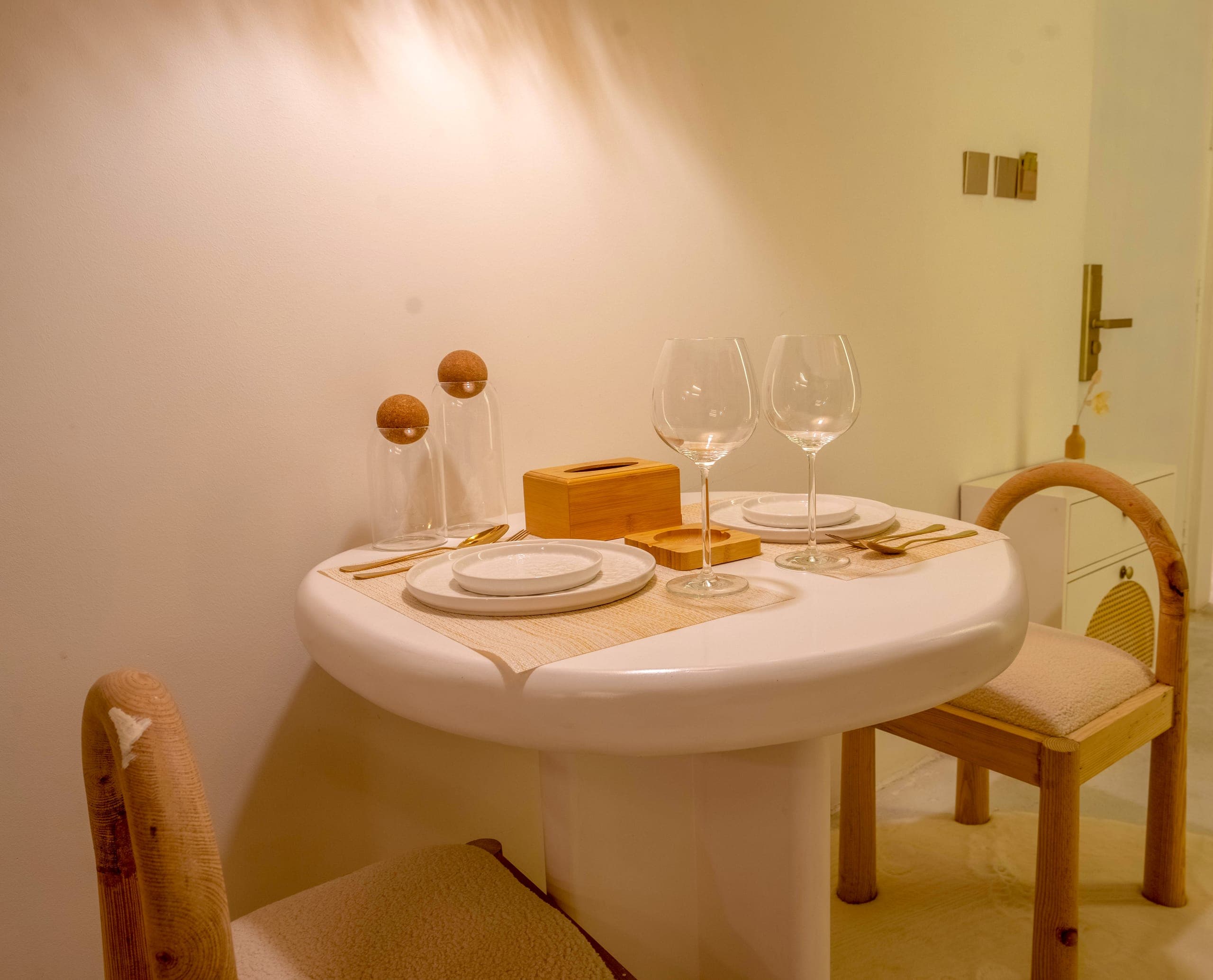 A round white table set for two with wine glasses and oak chairs in the Studio