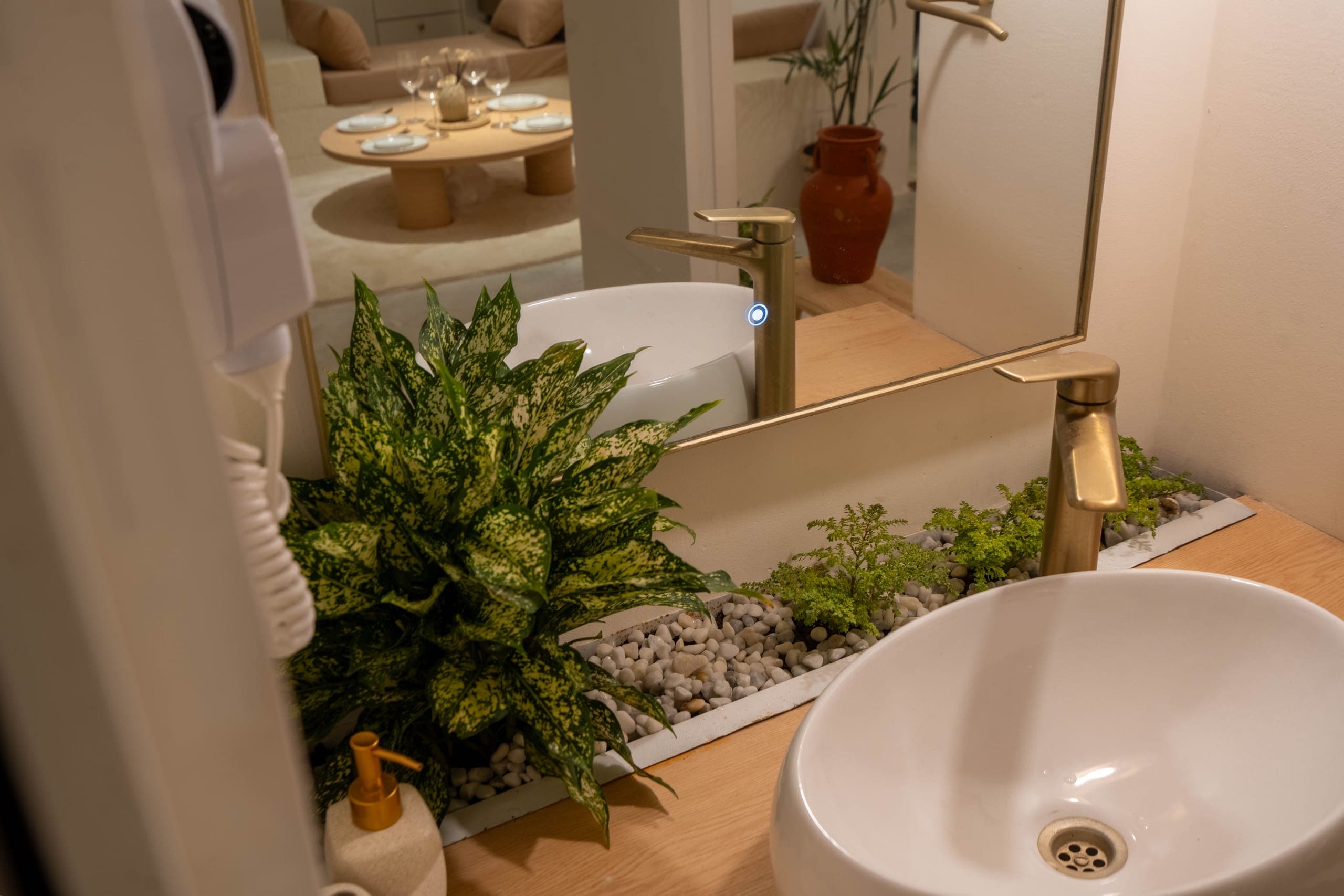 Vessel basin and brass taps on an oak vanity with a pebble planter, the hall reflected in the mirror