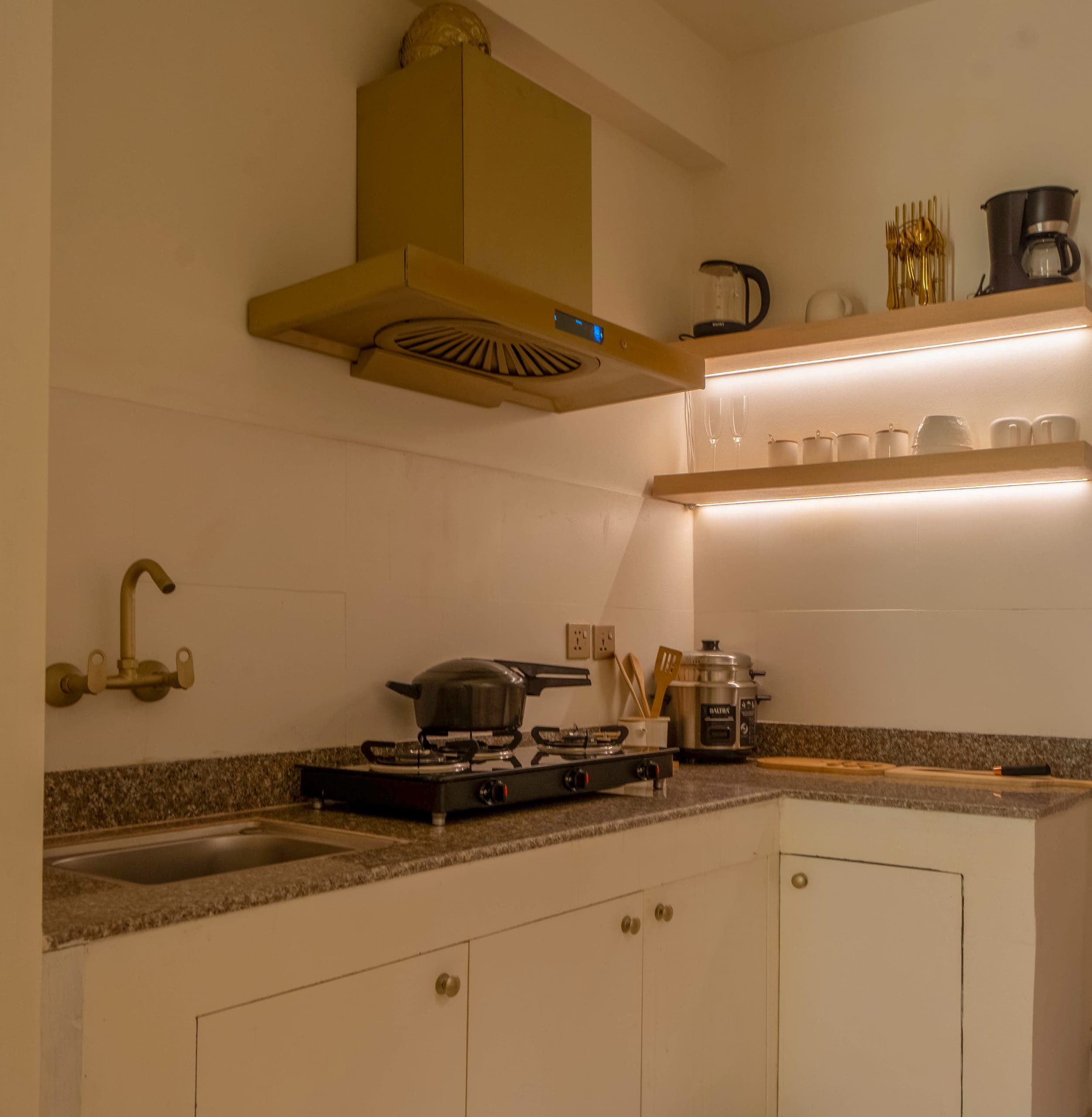 Studio kitchenette with a brass hood, a gas hob, a granite counter and lit open shelves