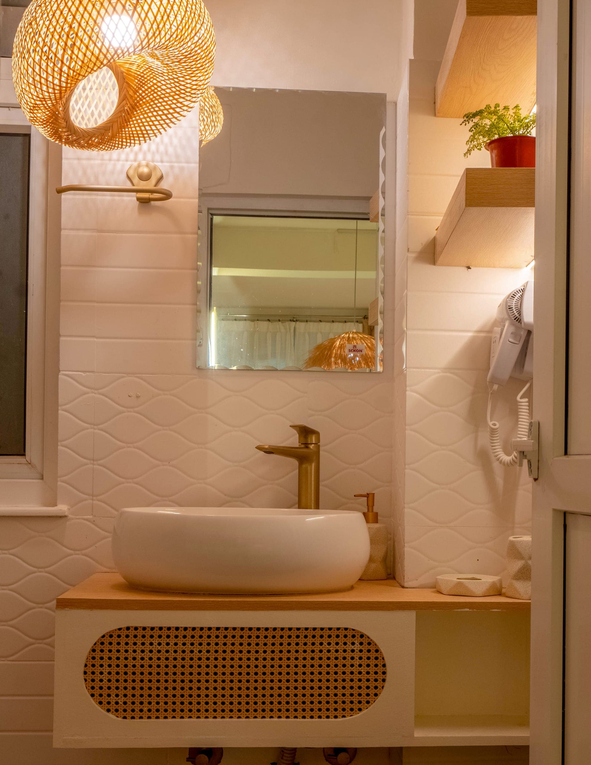 Studio bathroom: a vessel basin on a rattan-front vanity, a woven pendant and a backlit mirror