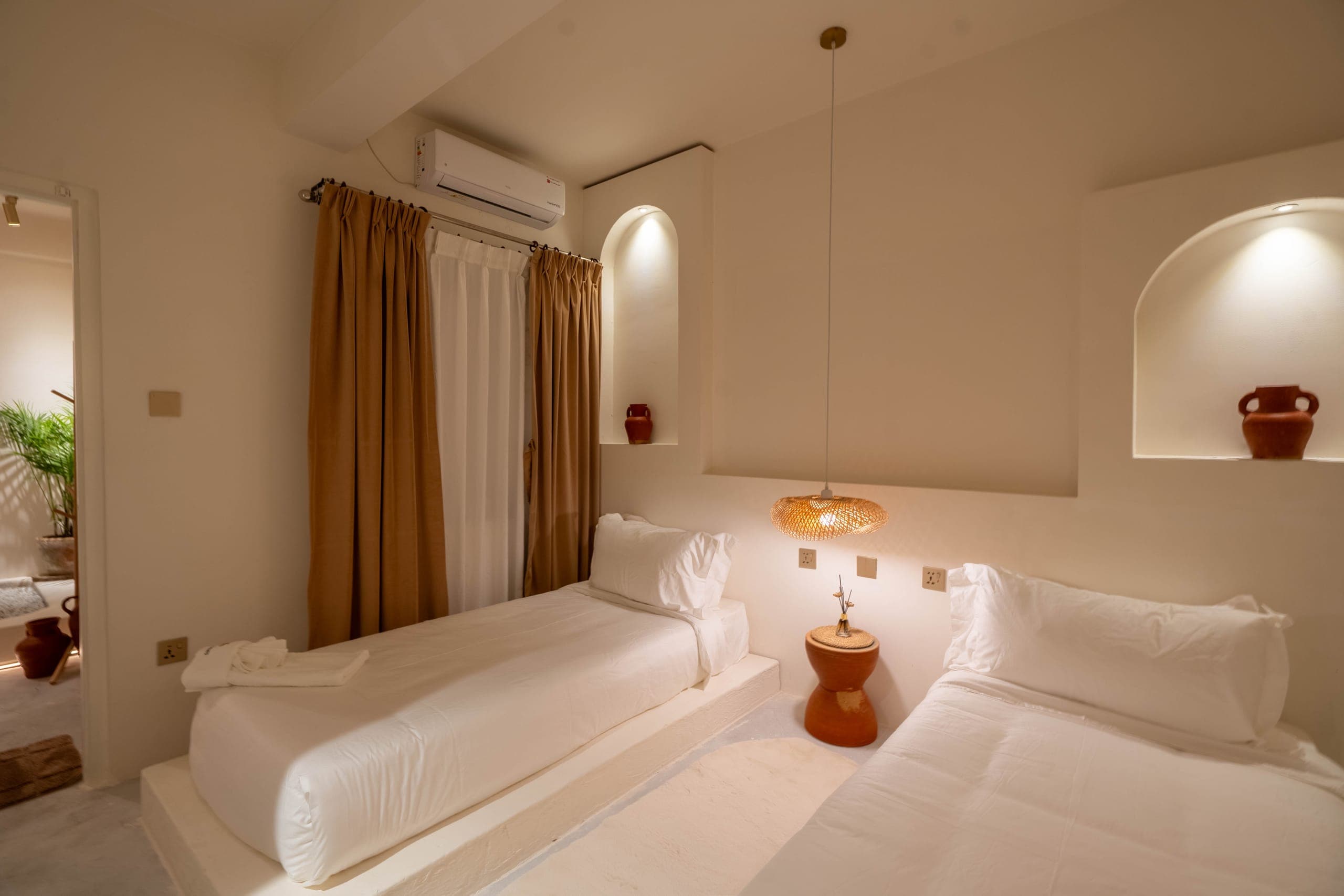 Twin bedroom with two white beds, plaster niches with terracotta jugs and linen curtains