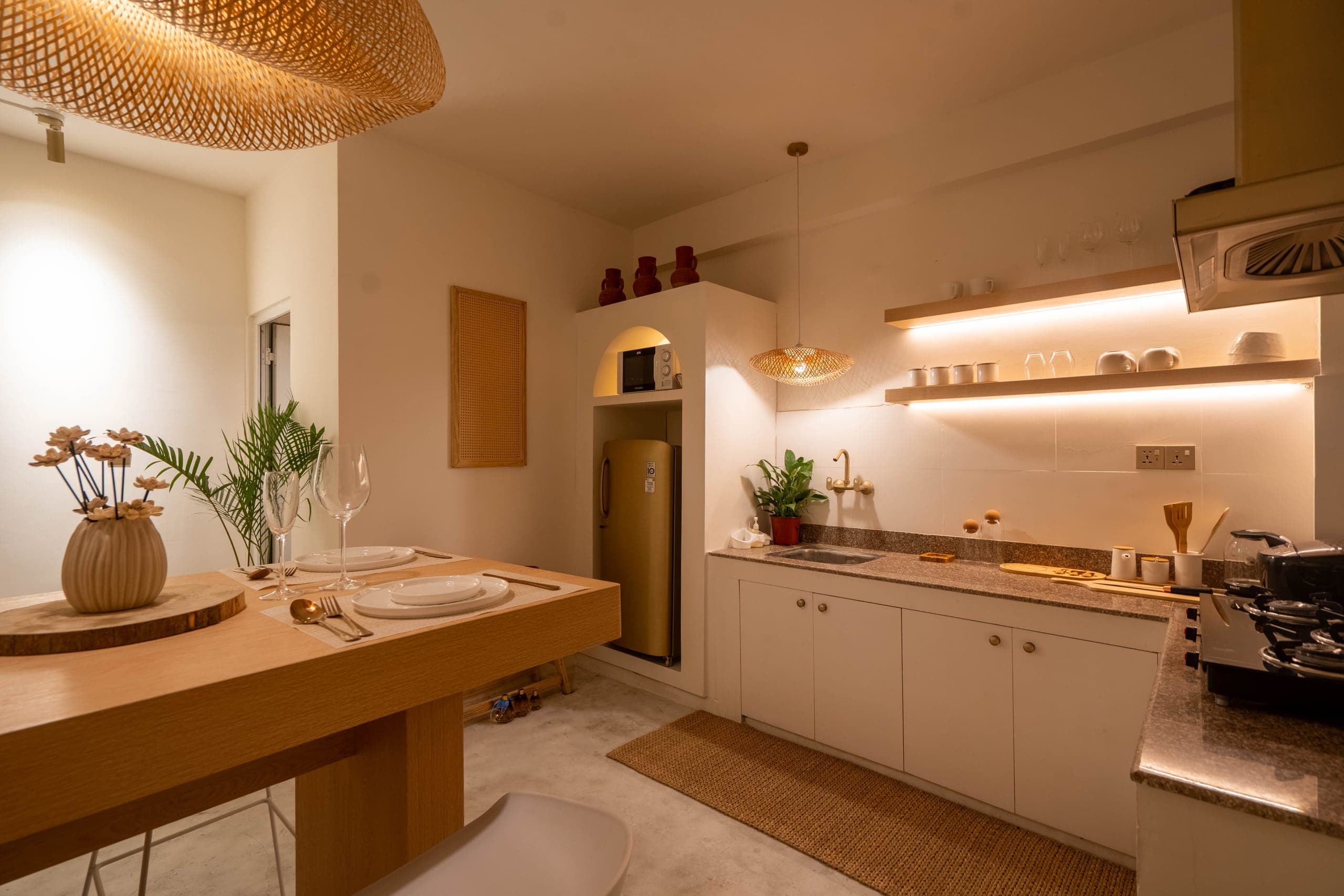 Oak dining table set for two in front of the suite's kitchen with lit open shelves and a gold fridge