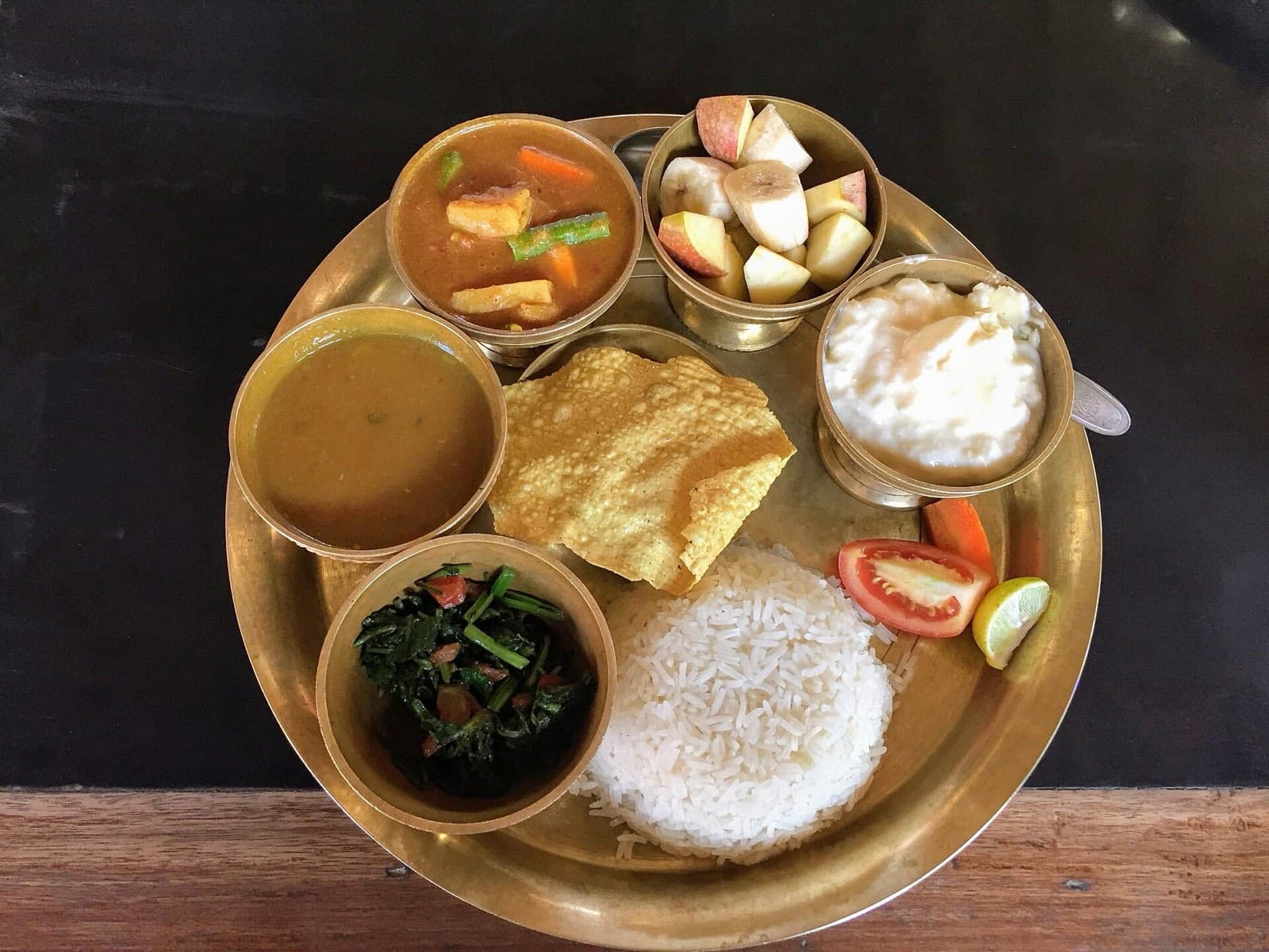 Dal bhat on a brass thali: rice, lentil soup, greens, vegetable curry, papad, yoghurt and fruit