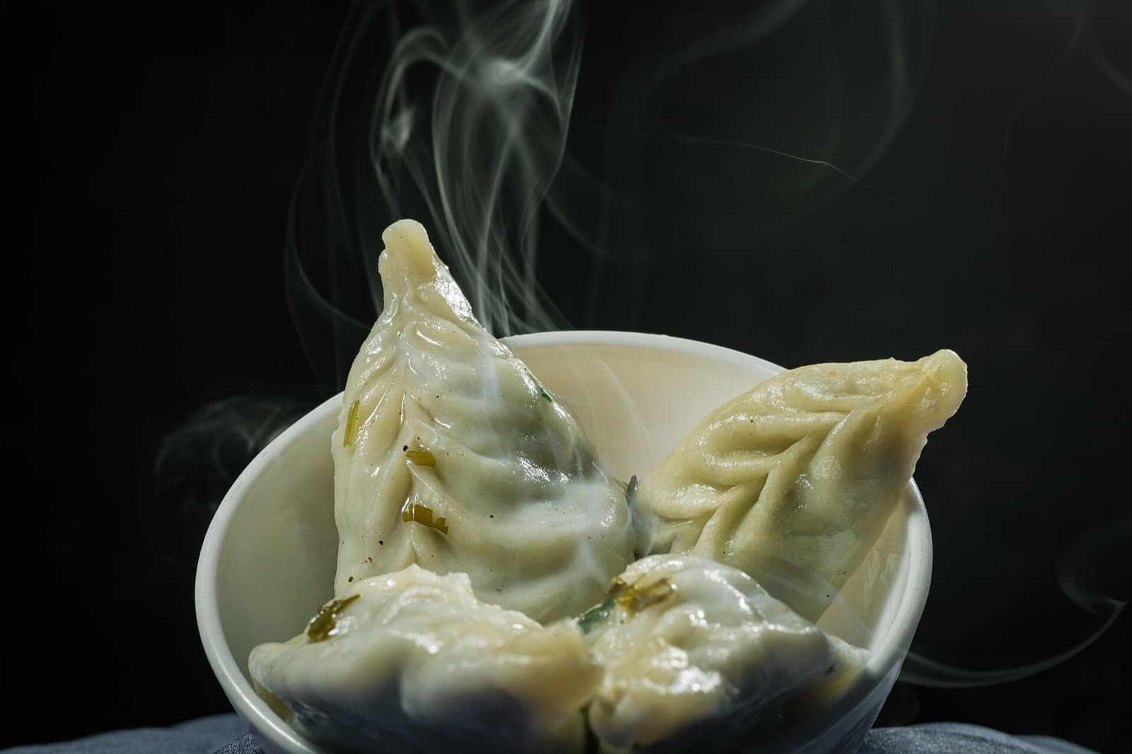 Steamed momo dumplings in a white bowl, steam rising against a dark background