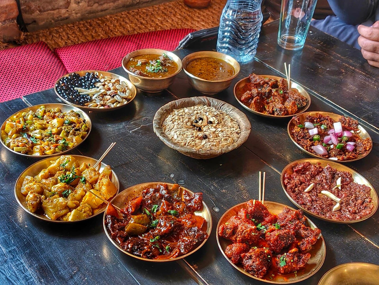 A Newari feast in brass bowls on a dark wooden table: beaten rice, choila, spiced potatoes, soybeans and curries
