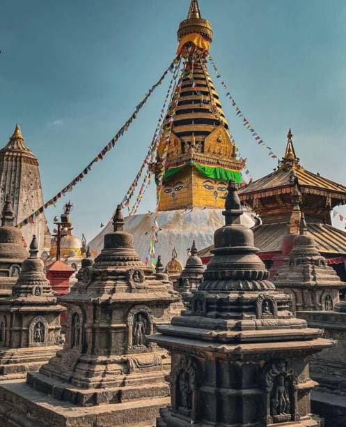 The golden spire and painted Buddha eyes of Swayambhunath Stupa behind carved stone shrines and prayer flags